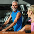 An older man and woman exercising in a gym with a Curcumin + CoQ10 Astaxant bottle nearby.