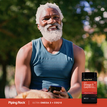 Older man smiling outdoors, holding a phone and a bottle of Ultra Omega + CoQ10 supplement.