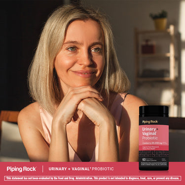 A smiling middle-aged woman rests her chin on her hands next to a bottle of Urinary + Vaginal Probiotic.