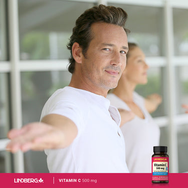 A middle-aged man is stretching while holding a Vitamin C bottle, showcasing an active lifestyle and health focus.
