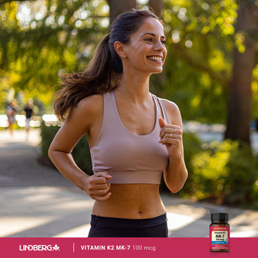 A young adult woman is jogging outdoors while holding a Vitamin K2 MK-7 bottle.