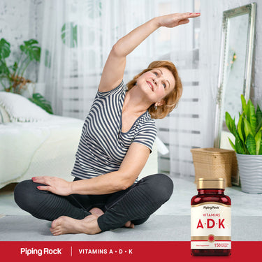 An elderly woman stretches on a mat next to a bottle of Vitamins A, D, and K.