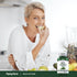 A mature woman smiles while eating an apple slice next to a bottle of Wild Lettuce.