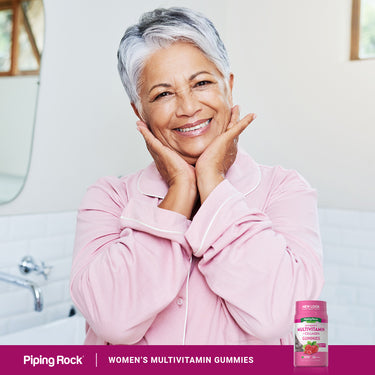 Senior woman smiling while holding a bottle of Women's Multivitamin Gummies in a lifestyle setting.