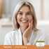 Middle-aged woman smiling, touching her cheek, beside a jar of Glycolic Acid Cream.