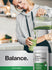 Lifestyle image of woman pouring a green smoothie into a glass with Horbäach Organic Super Greens Powder bottle nearby, stating Balance.
