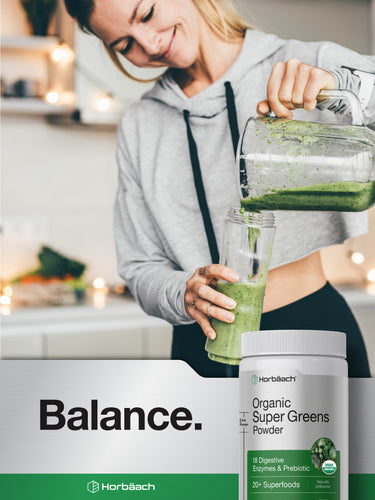 Lifestyle image of woman pouring a green smoothie into a glass with Horbäach Organic Super Greens Powder bottle nearby, stating Balance.