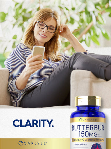Middle-aged woman smiling at her phone on a couch, next to a Butterbur bottle.
