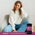 Young woman smiling in an armchair with a bottle of Multi Collagen Peptides beside her.