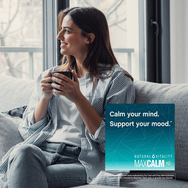 Young woman on couch with a mug, gazing out a window with a MaxCalm graphic.