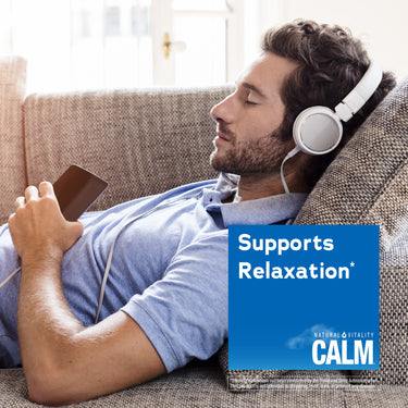 Man relaxing on couch with headphones and phone, next to Natural Vitality Calm.