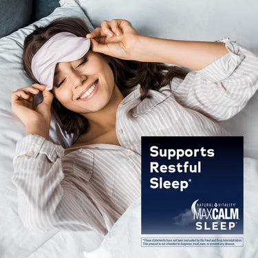 Young woman smiling in bed, removing a sleep mask, with an overlay for Natural Vitality MaxCalm Sleep.