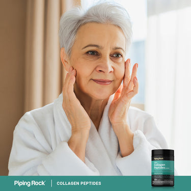 Adult touching facial skin while wearing a white robe with a Piping Rock Ultra Collagen Peptides Complex bottle nearby.