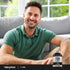 Adult smiling while seated indoors, with a Piping Rock Mega T1000 Standardized Tribulus Terrestris supplement bottle nearby
