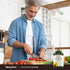 A middle-aged man chops tomatoes in a kitchen, with a bottle of Sunflower Lecithin nearby.