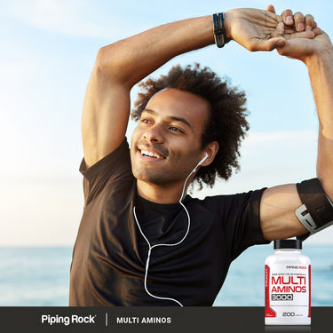 Active lifestyle image of an adult stretching outdoors while wearing earbuds, with a Piping Rock Multi Aminos 3000, 200 caplets bottle displayed nearby.