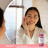 Lifestyle image of woman touching her face while looking in a mirror, with Piping Rock Hair, Skins & Nails supplement bottle nearby and small-print FDA disclaimer visible at bottom