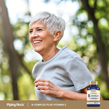 Adult smiling while walking outdoors, with a Piping Rock Complete B-Complex + Vitamin C bottle nearby