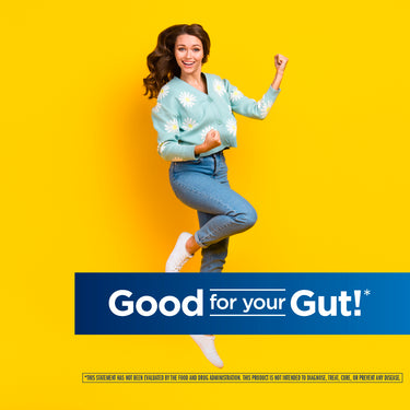 Young woman in a blue cardigan and jeans smiling and flexing near a banner saying 'Good for your Gut!'.