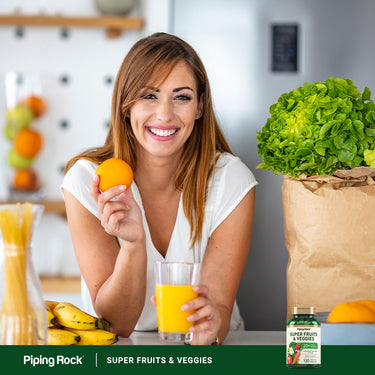 Woman smiling in a kitchen, holding an orange and juice, with Super Fruits & Veggies packaging visible.