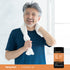 A middle-aged man smiles with a towel around his neck, standing beside a Vitamin D3 + K2 supplement bottle.